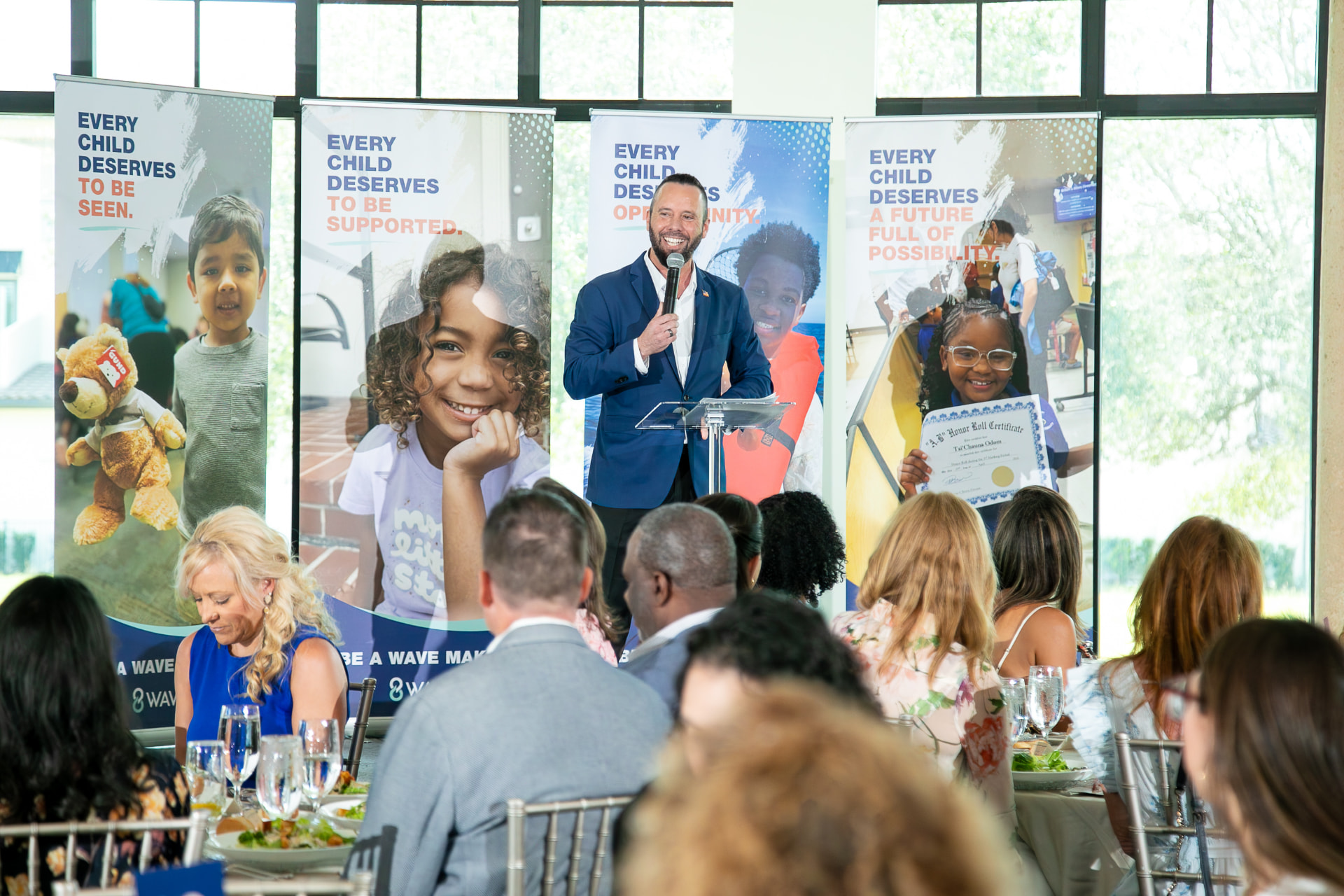 Austin Arthur speaking at the podium during the 2026 8 Waves WaveMaker Luncheon benefiting the I AM Children's Museum at Bella Collina